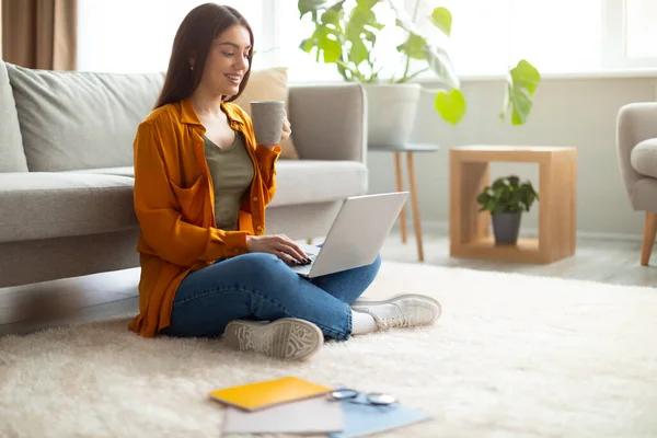 Glückliche Millennial Lady genießt Kaffee, während sie von zu Hause aus am Laptop arbeitet, leerer Raum — Stockfoto