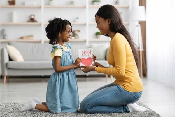 Mödrars dag koncept. Lilla afroamerikanska tjejen presenterar handgjort kort till mamma — Stockfoto