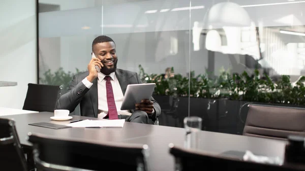 Empresario negro feliz usando tableta digital, hablando por teléfono — Foto de Stock