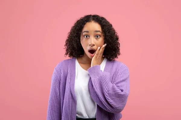 Megdöbbent fiatal afro-amerikai nő megérinti az arcát, és nézi a kamera meglepetés felett rózsaszín stúdió háttér — Stock Fotó