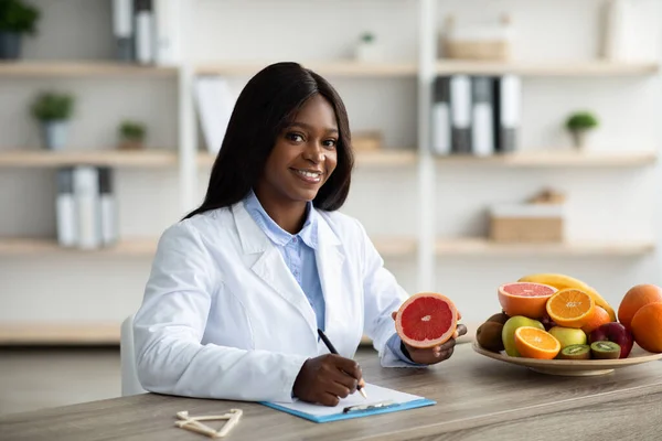 Dietista femenina alegre haciendo plan de comidas para el cliente, trabajando en la clínica de pérdida de peso, sonriendo a la cámara —  Fotos de Stock