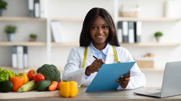 Nutritionniste afro-américaine positive avec presse-papiers créant un plan de repas à base de plantes pour le patient, panorama — Photo