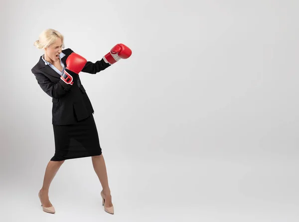 Geschäftserfolgskonzept. Junge Unternehmerin in Boxhandschuhen streikt, steht auf hellem Hintergrund — Stockfoto