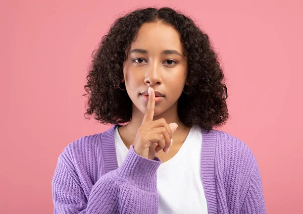 Cala-te, informações confidenciais. Jovem afro-americano mulher gestos hush no fundo do estúdio rosa — Fotografia de Stock