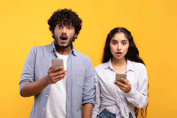 Omg. Geschokt Indiaas paar met behulp van smartphones en kijken naar camera met open mond over gele achtergrond, banner — Stockfoto