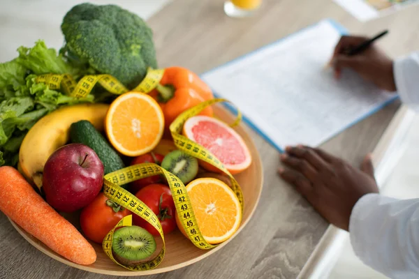 Питательница пишет план диеты со здоровыми овощами и фруктами на столе, здравоохранением и концепцией диеты — стоковое фото