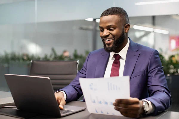 Feliz hombre de negocios negro revisando informes en la oficina moderna — Foto de Stock