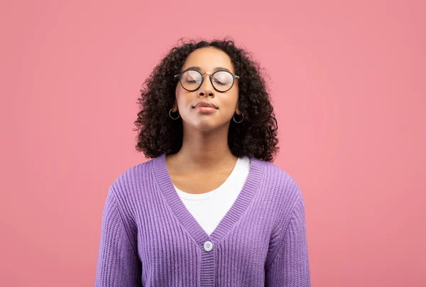 Calma joven mujer negra en gafas cerrando los ojos, respirando libremente sobre fondo rosa estudio — Foto de Stock