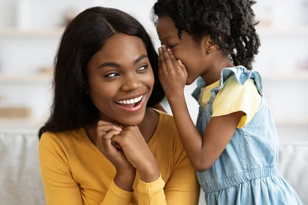 Γλυκό μικρό μαύρο κορίτσι ψιθυρίζει κάτι στο χαρούμενο αφτί της μαμάς της — Φωτογραφία Αρχείου