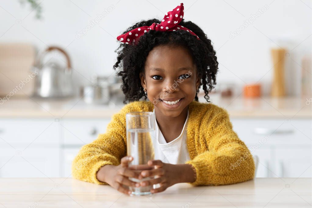 Cute Little Black Girl Holding Glass With Water While Sitting In Kitchen