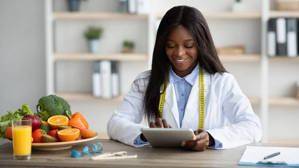 Junge Diätassistentin arbeitet mit Tablet-Computer, gibt Online-Beratung oder erstellt Diätplan im Büro — Stockfoto