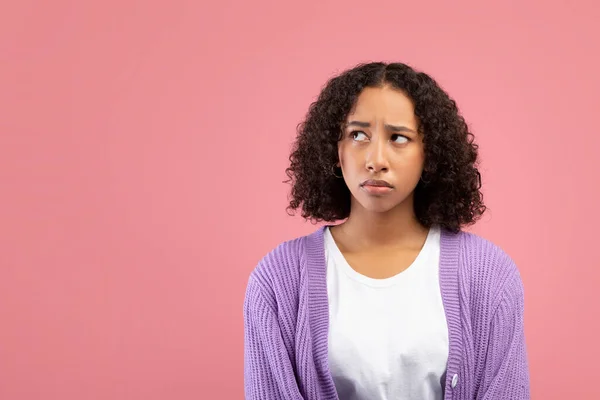 Przemyślana młoda czarna kobieta spogląda na puste miejsce na różowym tle studia — Zdjęcie stockowe