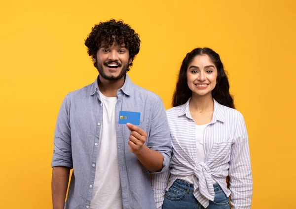 Paiements faciles sans contact. Heureux couple indien avec carte de crédit souriant à la caméra, posant sur fond jaune studio — Photo