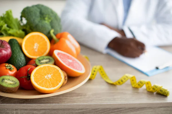 Υγιεινή και διατροφή. Γυναίκα διαιτολόγος γράφει σχέδιο διατροφής, κάθεται στο τραπέζι με λαχανικά και φρούτα στο πιάτο — Φωτογραφία Αρχείου