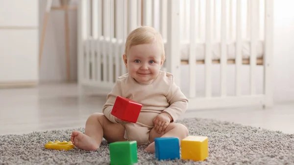 Portret van schattige kleine baby lachend naar de camera, spelend met kleurrijke blokjes, rustend op de vloer in de kinderkamer, panorama — Stockfoto