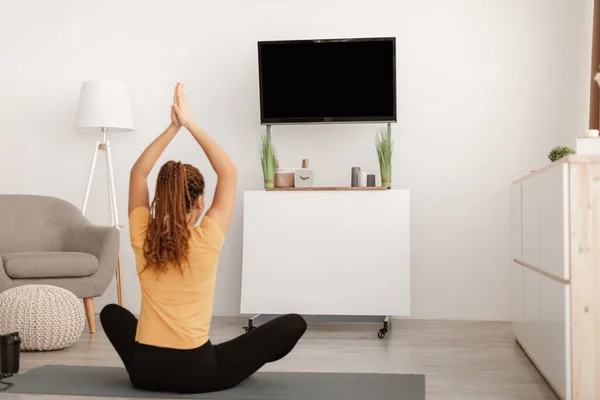 Mujer haciendo yoga sentada en posición de loto viendo televisión en interiores — Foto de Stock