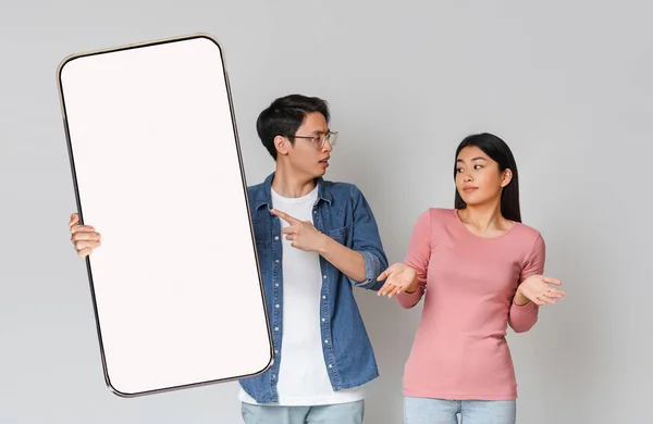 Angry Asian man showing white empty smartphone screen to wife