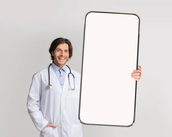 Médico sosteniendo gran pantalla vacía de teléfono inteligente blanco, maqueta — Foto de Stock