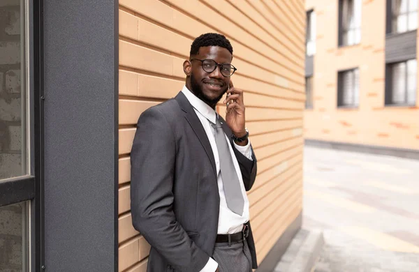 Αυτοπεποίθηση αφροαμερικανός επιχειρηματίας έχει συνομιλία σε εξωτερικούς χώρους smartphone, με τα πόδια στην πόλη κοντά σε κτίρια γραφείων — Φωτογραφία Αρχείου