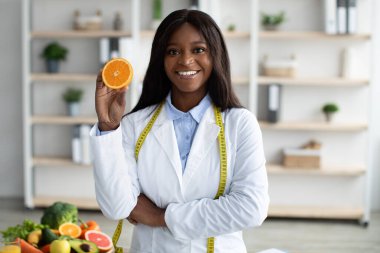 C vitamini bağışıklık için iyidir. Mutlu Afro-Amerikan diyetoloğu elinde portakal yarısıyla taze meyve yemeyi öneriyor.