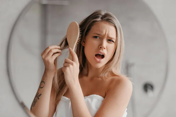 Σκέψη αποκόλλησης μαλλιών. Θυμωμένη κυρία βούρτσισμα ξηρά μαλλιά με βούρτσα μαλλιών, που πάσχουν από πόνο κατά τη διάρκεια της ρουτίνας ομορφιάς — Φωτογραφία Αρχείου