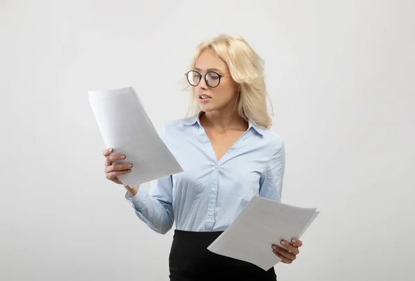 Mujer de negocios seria en ropa formal y anteojos leyendo documentos sobre fondo de estudio gris claro — Foto de Stock