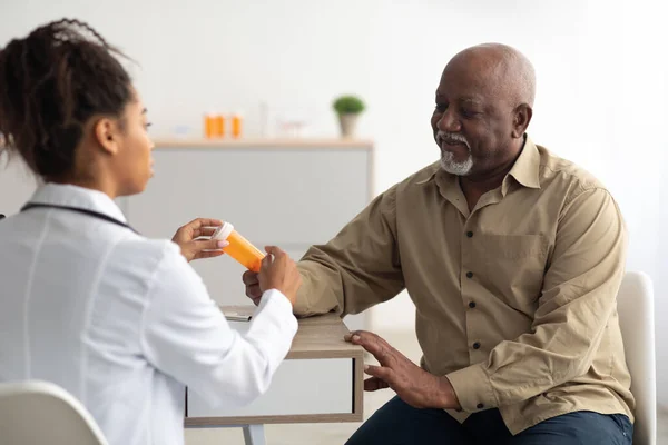 Médica negra mostrando pílulas para paciente do sexo masculino — Fotografia de Stock