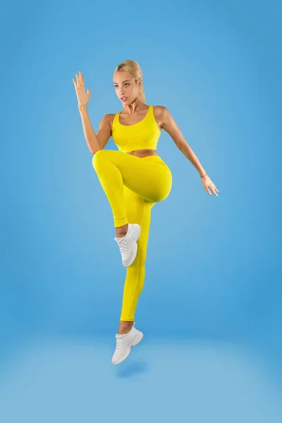 Mujer joven saltando y haciendo ejercicio aislado sobre fondo azul —  Fotos de Stock