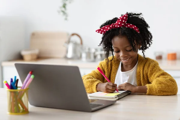 Estudo afro-americano pequeno bonito da menina com portátil e escrita no bloco de notas — Fotografia de Stock