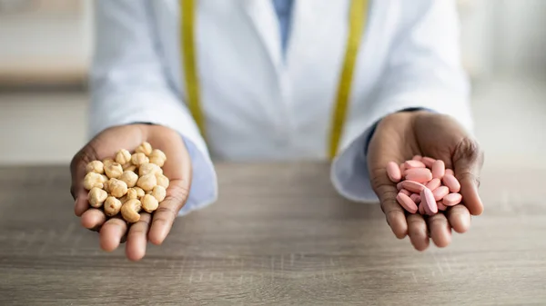 Nutrición saludable vs concepto de medicación. Dietista femenina sosteniendo tabletas y nueces en la mesa en la clínica, vista de cerca — Foto de Stock