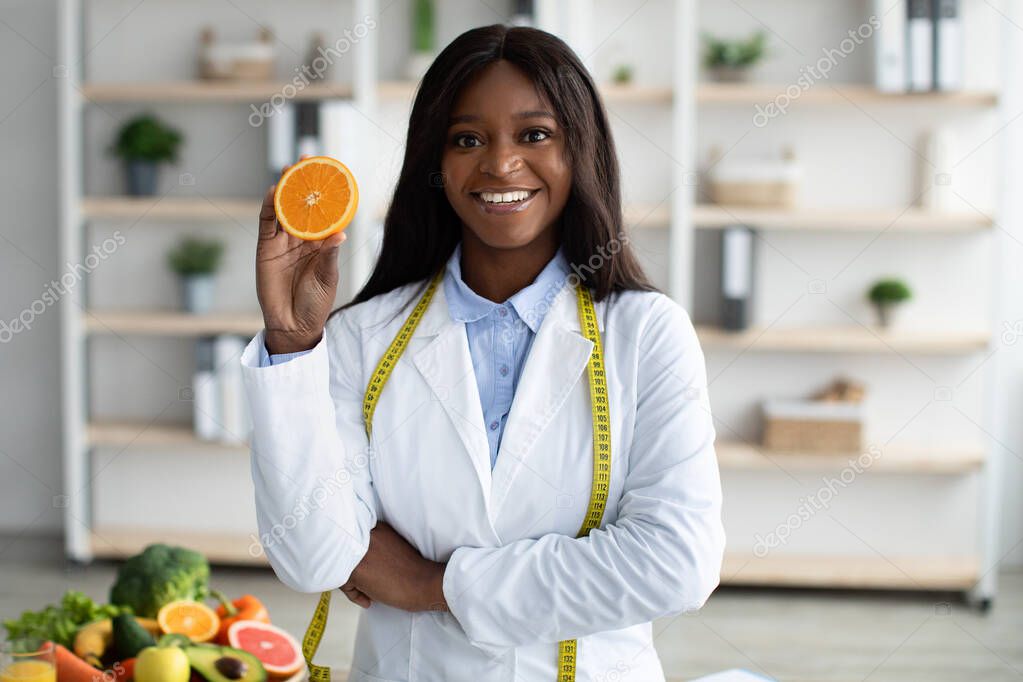 Vitamin C is good for immunity. Happy african american dietologist holding orange half, recommending fresh fruits to eat