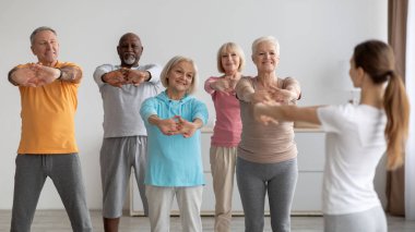 Sportif yaşlılar fitness kursuna gidiyor, eğitmenle eğitim görüyor.