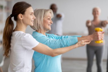 Spor yaparken yaşlı bir kadına yardımcı olan spor koçunun yan görüntüsü