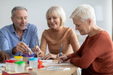 Olumlu yaşlı erkek ve kadınlar fırçayla resim yapmaktan zevk alıyorlar