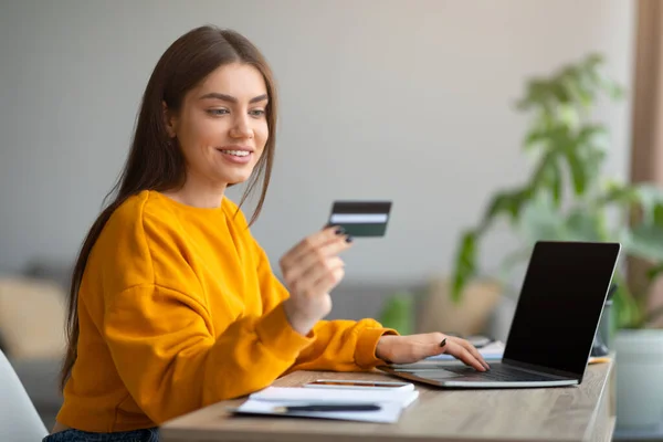 Krásná mladá žena držící kreditní kartu a pomocí notebooku s prázdnou obrazovkou, nakupování on-line doma, mokup pro webové stránky — Stock fotografie