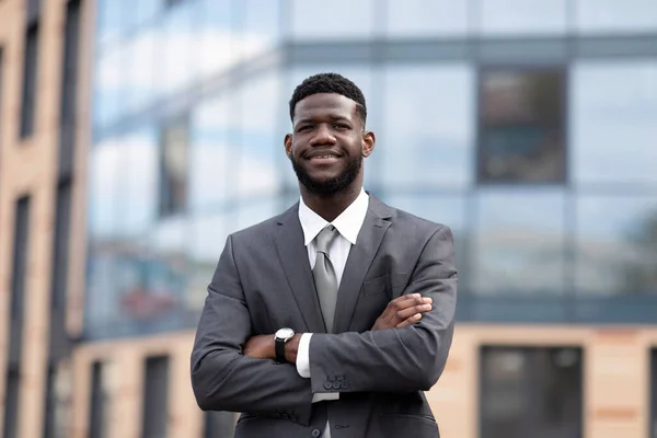Πλούσιος αφροαμερικάνος επιχειρηματίας νεαρός άνδρας που στέκεται έξω από το σύγχρονο κτίριο γραφείων, ποζάροντας με διπλωμένα χέρια — Φωτογραφία Αρχείου