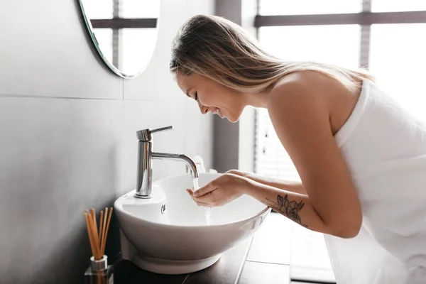 Jonge dame wassen gezicht en genieten van ochtend gezichtsverzorging routine na het wakker worden, badkamer interieur — Stockfoto