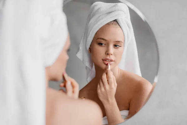 Dagelijkse schoonheidsroutine. Mooie jonge vrouw aanbrengen van lippenstift en kijken naar spiegel, met behulp van natuurlijke decoratieve cosmetica — Stockfoto