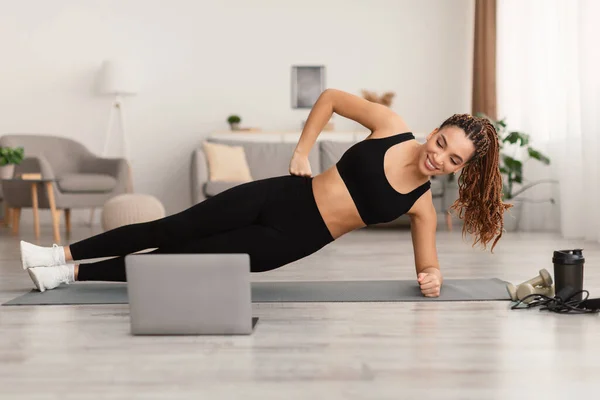 Sportig dam gör Side Plank Motion nära laptop hemma — Stockfoto