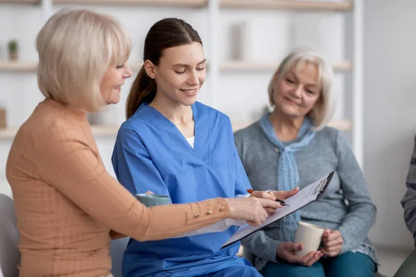 Hübsche junge Krankenschwester befragt ältere Damen im Pflegeheim — Stockfoto