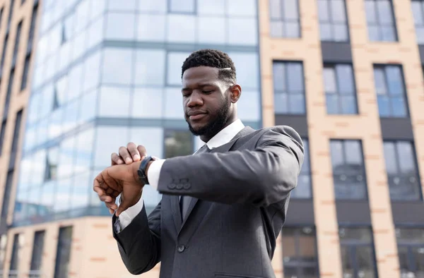 Tidsplanering. Fokuserad afrikansk amerikansk affärsman tittar på armbandsur, promenader under paus i centrum — Stockfoto