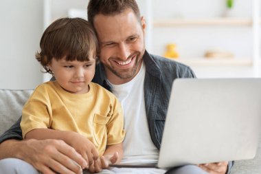 Modern teknolojiler ve çocukluk. Mutlu küçük çocuk evde gülen babasıyla birlikte dizüstü bilgisayarda dijital televizyon izliyor.
