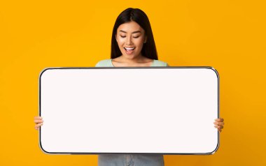 Neşeli Asyalı kadın büyük beyaz, boş akıllı telefon ekranı gösteriyor.