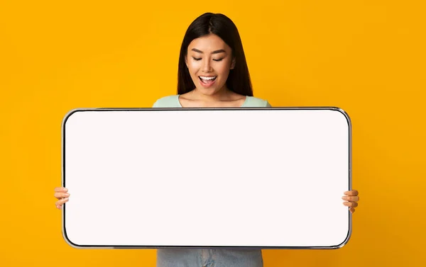 Весела азіатка показує великий білий порожній екран смартфона — стокове фото