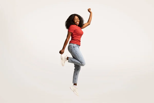 Беззаботная молодая черная женщина прыгает в воздух и смотрит в камеру — стоковое фото