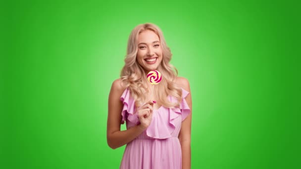 Playful Blonde Female Eating Lollipop And Having Fun, Green Background — Stock Video