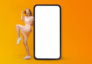 Boş ekranlı akıllı telefonun yanında EVET işareti yapan, online piyango ya da kumarhane bahsini kazanan öforik genç kadın.