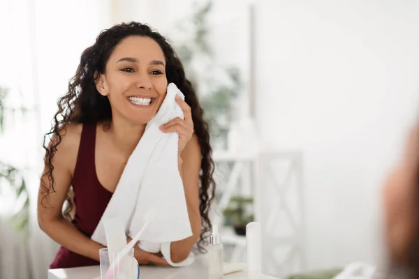 Schöne junge Frau genießt die morgendliche Beauty-Routine, wischt sich das Gesicht mit einem Handtuch ab, steht zu Hause vor dem Spiegel — Stockfoto