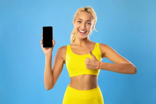 Χαρούμενη σπορ γυναίκα δείχνει κινητό τηλέφωνο με λευκή οθόνη — Φωτογραφία Αρχείου