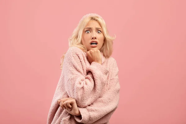 Skräckslagen ung dam som känner sig rädd, försöker gömma sig, står på rosa bakgrund, tittar på kamera med vidöppna ögon — Stockfoto